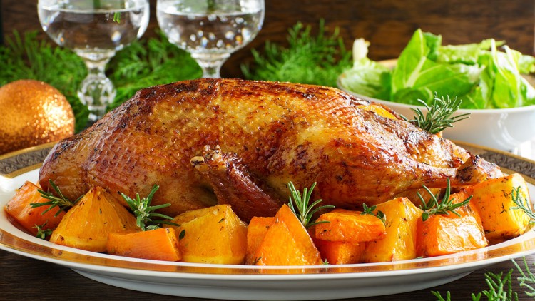 Gebratene Ente mit goldbrauner Kruste, umgeben von Orangenspalten, Rosmarin und Kräutern auf einem weißen Porzellanteller.
