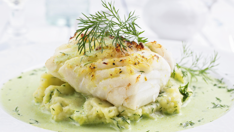 Ein gebratenes Fischfilet auf Kartoffelpüree mit grüner Soße und Dillzweigen auf einem weißen Teller.