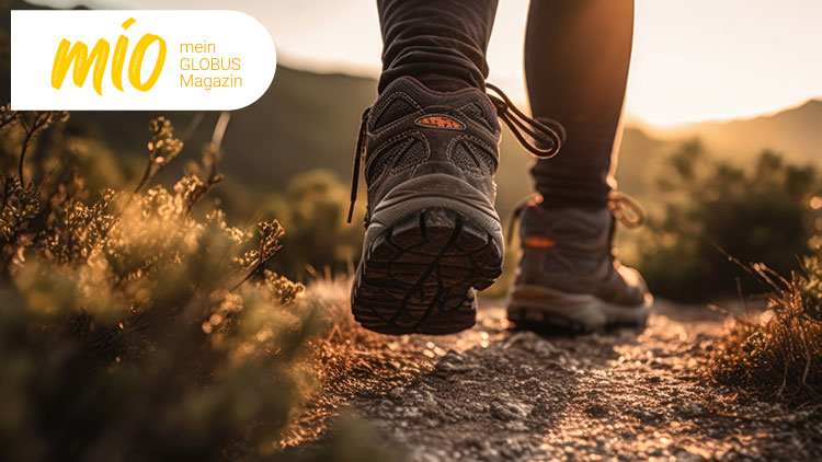 Ein Paar Wanderschuhe auf einem unbefestigten Weg in natürlicher Umgebung bei Sonnenuntergang, mio mein GLOBUS Magazin.