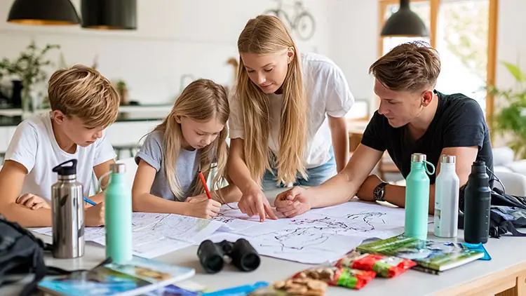 Vier Personen studieren eine Landkarte an einem Tisch mit Wasserflaschen, Fernglas, Snacks und Broschüren.