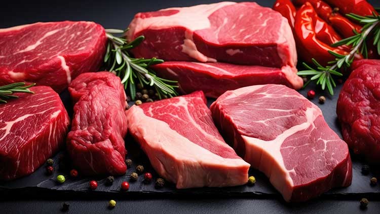 Verschiedene rohe Rindersteaks auf schwarzer Platte, garniert mit Rosmarinzweigen, Pfefferkörnern und roten Paprikaschoten.