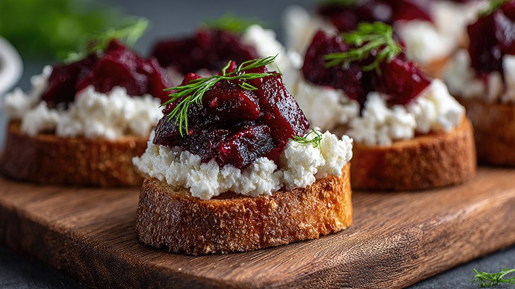 Geröstete Brotscheiben belegt mit Hüttenkäse, rotbraunen Rübenstücken und frischem Dill liegen auf einem Holzbrett.