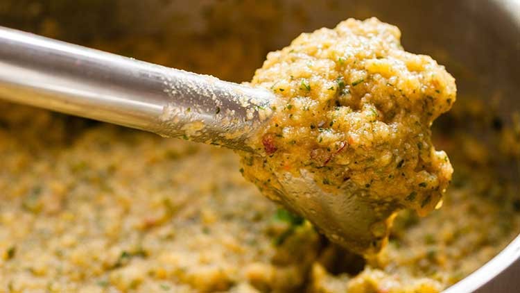 Ein Stabmixer hebt eine Portion cremiger, gelbgrüner Masse mit Kräutern und kleinen Gemüsestückchen aus einer Schüssel.