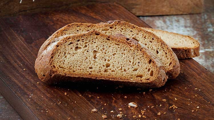 Mehrere Scheiben braun gebackenes Brot mit knuspriger Kruste liegen auf einem dunklen Holzbrett.