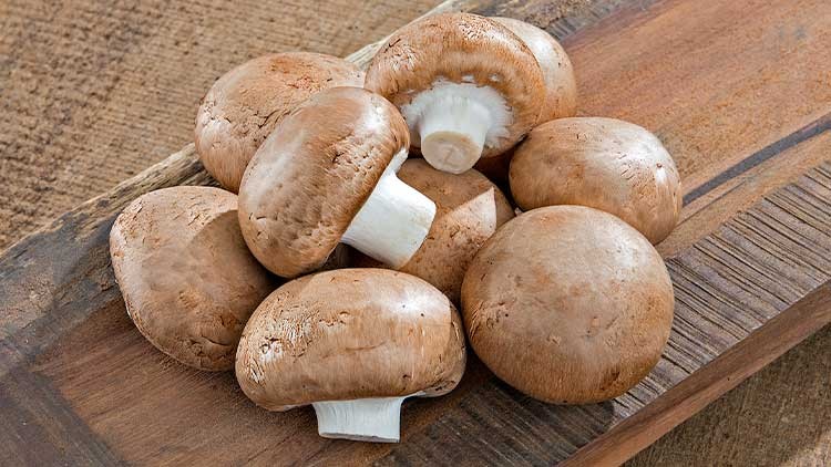 Mehrere braune Champignons liegen auf einem hölzernen Untergrund.