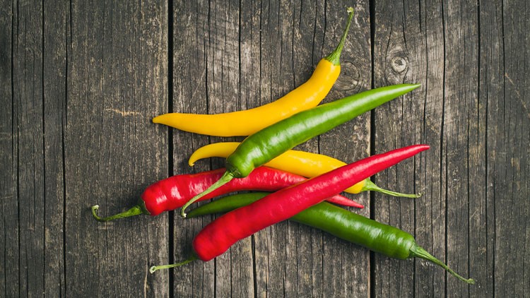 Rote, grüne und gelbe Chilischoten liegen auf einer rustikalen, dunklen Holzoberfläche.