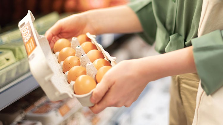 Eine Person hält geöffnete Eierverpackung mit braunen Eiern vor einem Verkaufsregal in einem Supermarkt.