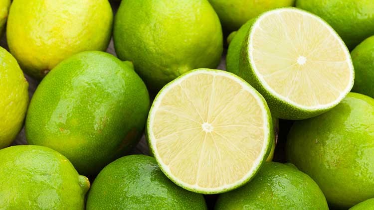 Grüne Limetten liegen nebeneinander, eine davon ist halbiert und zeigt die helle, saftige Frucht im Inneren.