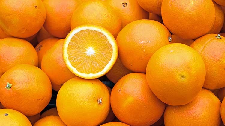Mehrere orangefarbene Orangen, von denen eine halbiert ist und ihre saftige, helle Fruchtfleischstruktur zeigt.