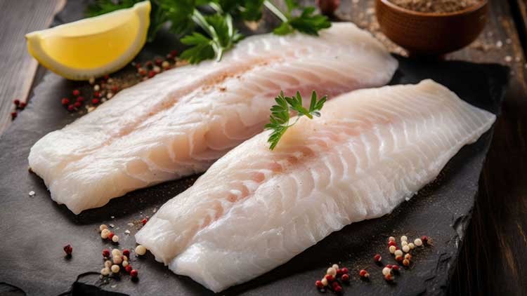 Zwei rohe Fischfilets mit Petersilie, bunter Pfeffermischung und einer Zitronenscheibe auf einer dunklen Schieferplatte.