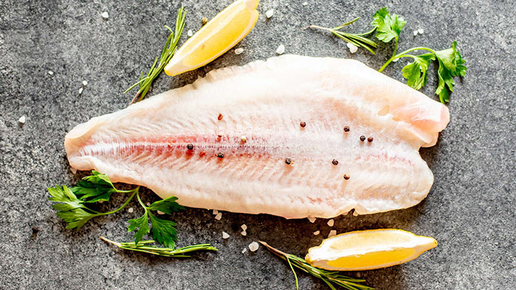 Ein rohes Fischfilet mit rosa Ader, dekoriert mit Pfefferkörnern, Petersilie, Zitronenspalten und grobem Salz auf grauem Untergrund.