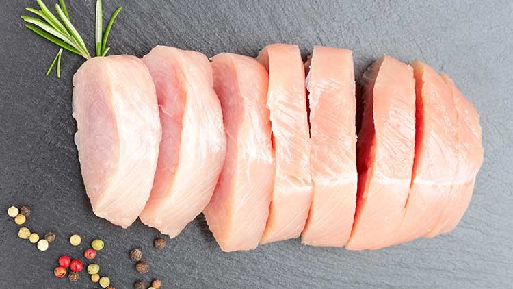 Mehrere Scheiben rohes, helles Fleisch liegen auf einer schwarzen Schieferplatte, dekoriert mit Rosmarinzweig und Pfefferkörnern.