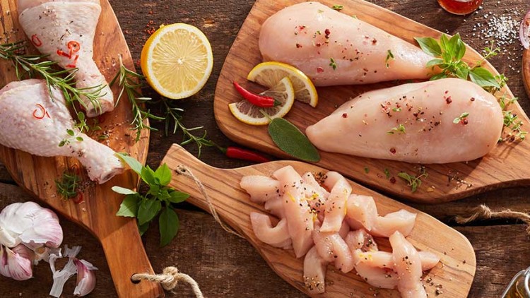 Frisches rohes Hähnchenfleisch, darunter Keulen, Brustfilets und Stücke, dekoriert mit Kräutern, Gewürzen und Zitronenscheiben.
