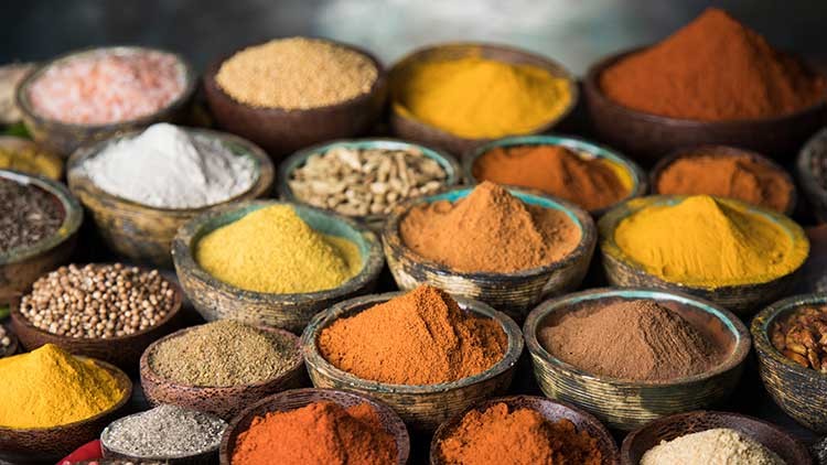 Verschiedene bunte Gewürze wie Kurkuma, Paprika und Curry sind in kleinen Holzschalen nebeneinander angeordnet.