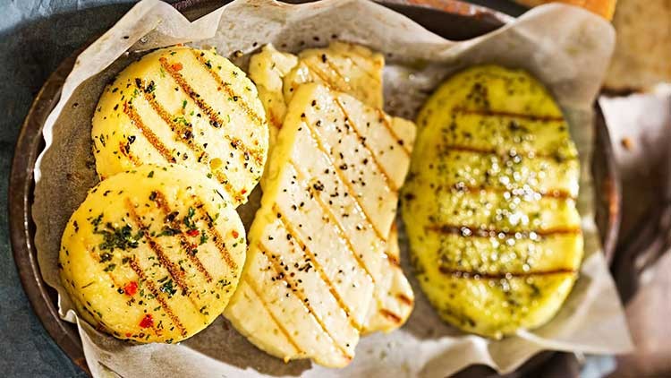 Gegrillter Halloumi und Gemüsefrikadellen mit Kräutern und Gewürzen auf Backpapier in einer Metallpfanne angerichtet.