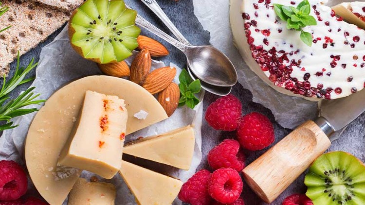 Verschiedene Käsesorten, Himbeeren, Kiwi, Mandeln, Cracker und Konfitüre auf einem gedeckten Tablett mit einem Messer.