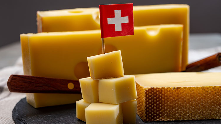 Käsestücke und Käsewürfel mit einer roten Fahne mit weißem Kreuz, Holzmesser und Tücher im Hintergrund.