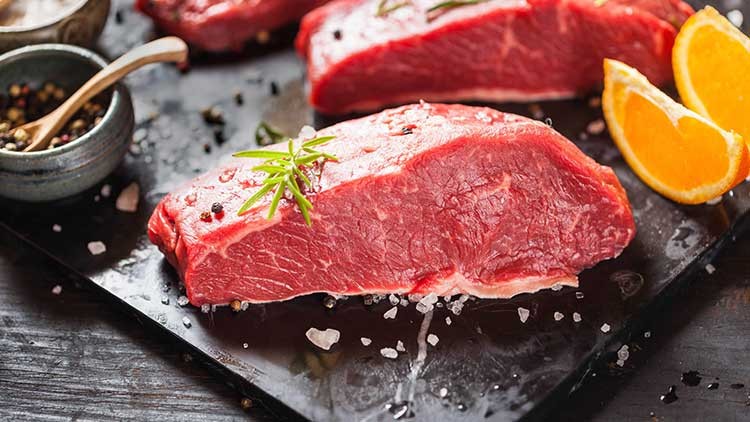 Rohes Rindersteak auf schwarzer Platte mit Rosmarinzweig, grobem Salz, Pfefferkörnern und Orangenscheiben dekoriert.