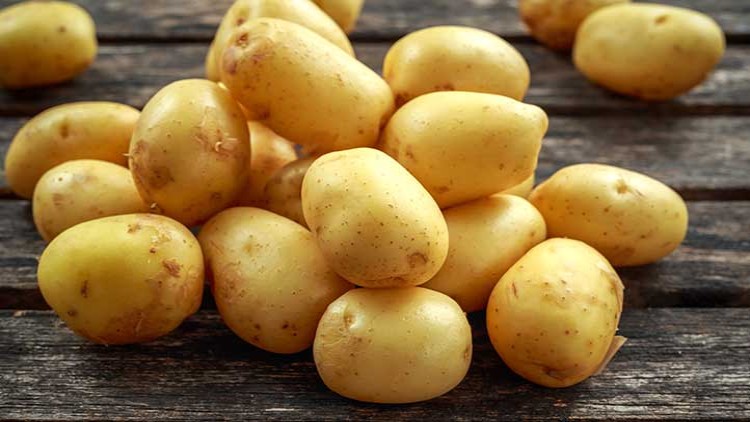 Mehrere ungekochte, gelbe Kartoffeln liegen auf einer hölzernen Oberfläche.