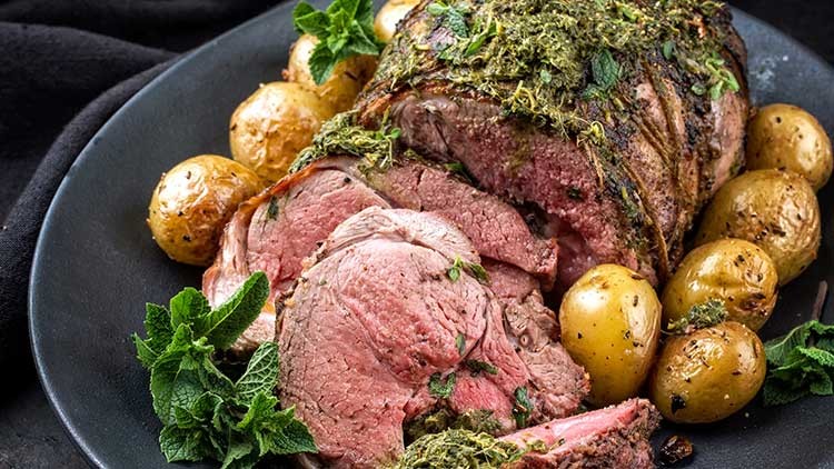 Ein Teller mit gebratenem Fleisch, frischen Kräutern, kleinen goldgelben Kartoffeln und Minzblättern als Garnitur.