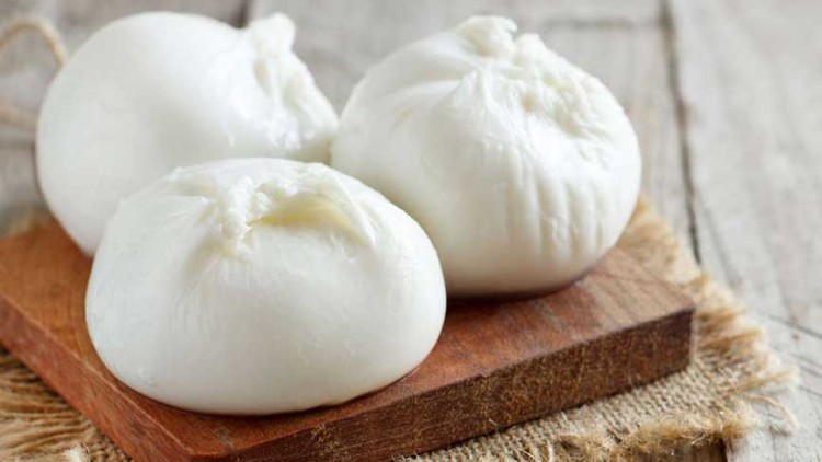 Drei weiße Kugeln aus Mozzarella liegen auf einem Holzbrett, das auf einem hellen rustikalen Untergrund liegt.