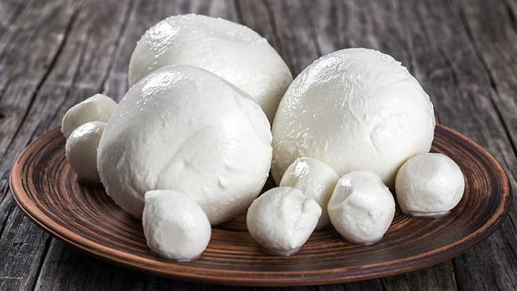 Weiße Mozzarella-Kugeln in unterschiedlichen Größen liegen auf einem braunen Teller mit Holzmaserung, Hintergrund aus Holz.