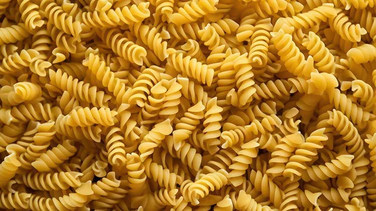 Viele ungekochte, gelbliche Fusilli-Nudeln liegen dicht nebeneinander und füllen das ganze Bild aus.