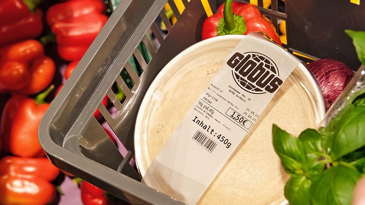 Grauer Einkaufskorb mit roter Paprika, Basilikum und Globus Verpackung mit 450 g Inhalt, Schriftzug GLOBUS auf dem Etikett.