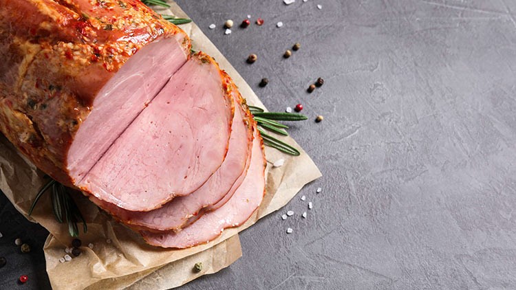 Aufgeschnittener Braten mit Kräutern und Gewürzen auf braunem Papier, daneben Rosmarinzweige, bunte Pfefferkörner und grobes Salz.