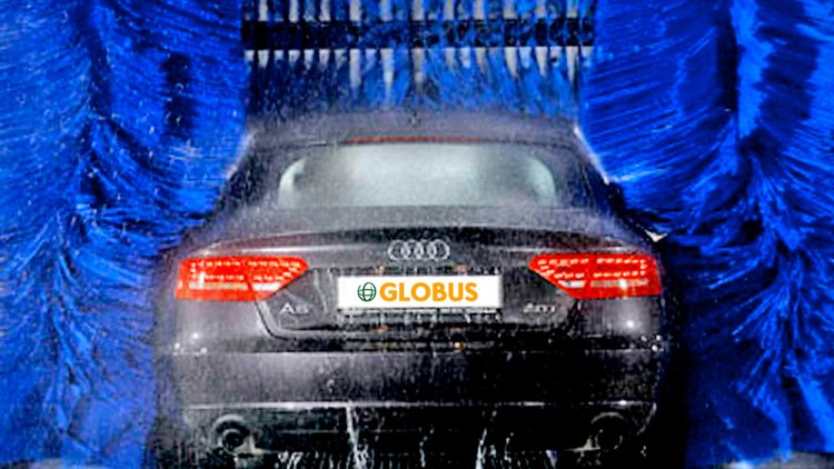 Ein schwarzes Auto mit GLOBUS-Kennzeichen wird in einer Waschanlage zwischen blauen Bürsten gereinigt.