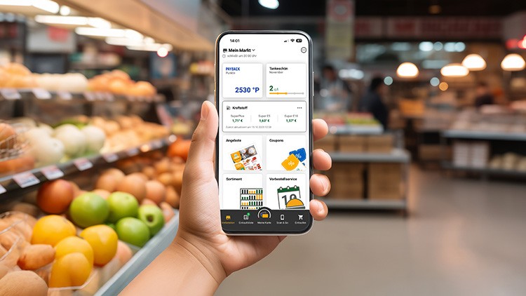 Hand hält Smartphone, auf dem eine App mit PAYBACK-Punkten, Angeboten, Coupons, Sortiments- und Vorteilsinfo angezeigt wird.