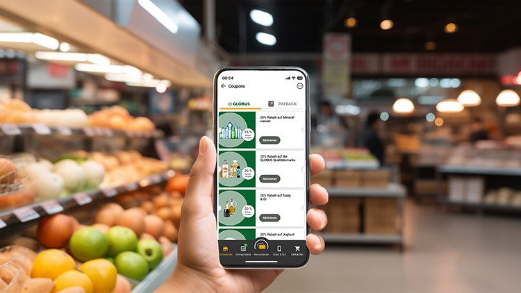 Hand hält Smartphone mit der GLOBUS App, auf dem Bildschirm sind Coupons und Angebote vor einer Obsttheke sichtbar.