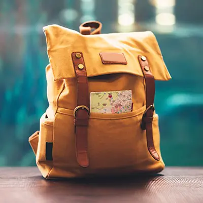 Gelber Rucksack mit braunen Lederdetails und eine Karte in der Außentasche, stehend auf einer Holzoberfläche.