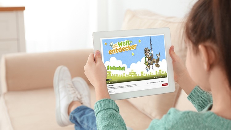 Kind hält ein Tablet, auf dem eine GLOBUS-Weltentdecker-Seite mit Globini und dem Titel „Steinobst“ angezeigt wird.