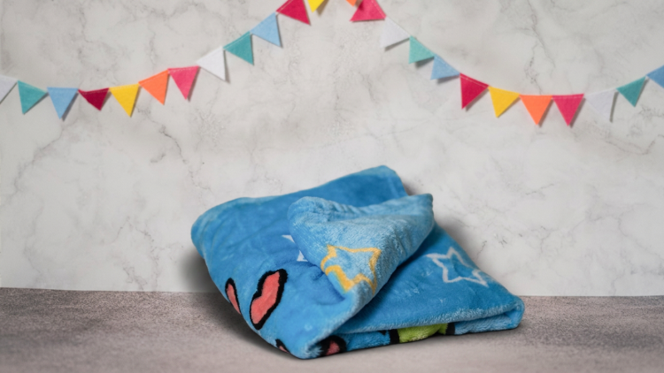 Gefaltete blaue Kuscheldecke mit Stern- und Herzmustern, im Hintergrund bunte Wimpel vor einer Marmorwand.
