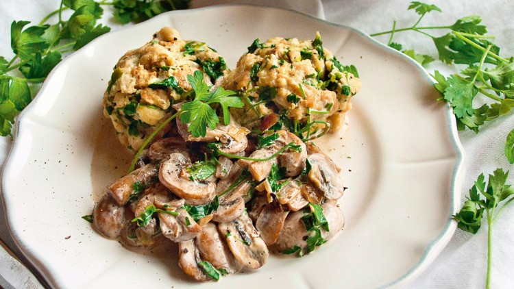 Auf einem weißen Teller liegen zwei Semmelknödel mit frischer Petersilie und Rahm-Champignons, umgeben von Petersilien-Dekoration.