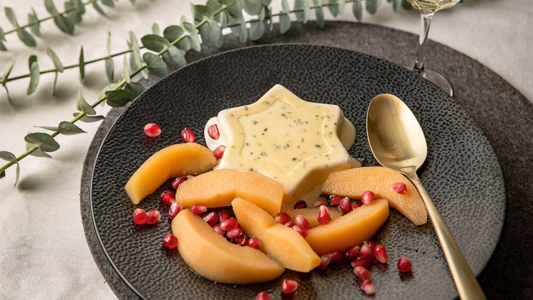 Schwarzer Teller mit sternförmigem Dessert, gebackenen Fruchtscheiben, Granatapfelkernen und goldenem Löffel, daneben Eukalyptus.