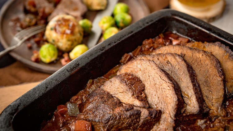 In einer rechteckigen schwarzen Auflaufform liegen mehrere Scheiben Braten in dunkler Soße mit Gemüsestücken.