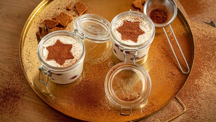 Drei kleine Gläser mit Mascarpone-Dessert, Kakaopulver in Sternform dekoriert, auf einem goldenen Tablett mit Kakaostaub.