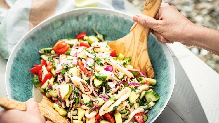 Große Schüssel mit gemischtem Salat aus Gurken, Tomaten, Zwiebeln und Kräutern wird mit Holzsalatbesteck gemischt.