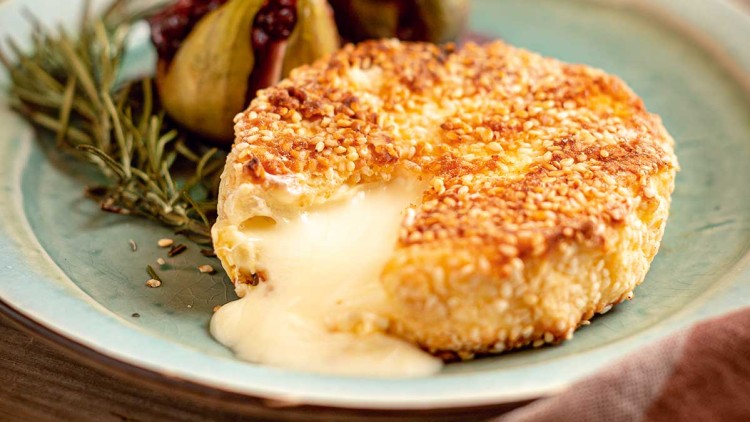 Ein goldbraun gebackener Käse mit fließendem Kern, angerichtet mit frischen Feigen, Rosmarin und Honig auf einem Teller.