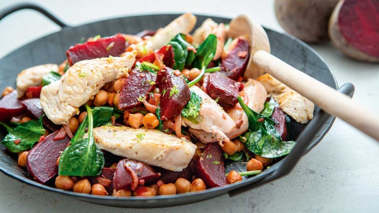 Gericht in einer schwarzen Pfanne mit Hähnchenfilet, Rote Bete, Kichererbsen, frischem Spinat und einem Holzlöffel.