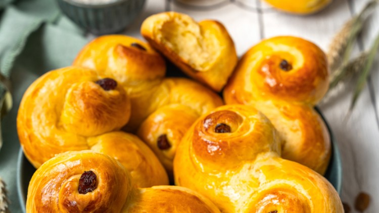 Leuchtend gelbe Hefebrötchen mit Rosinen auf blauem Teller, daneben Salzschale, grüne Serviette und Weizenähren.