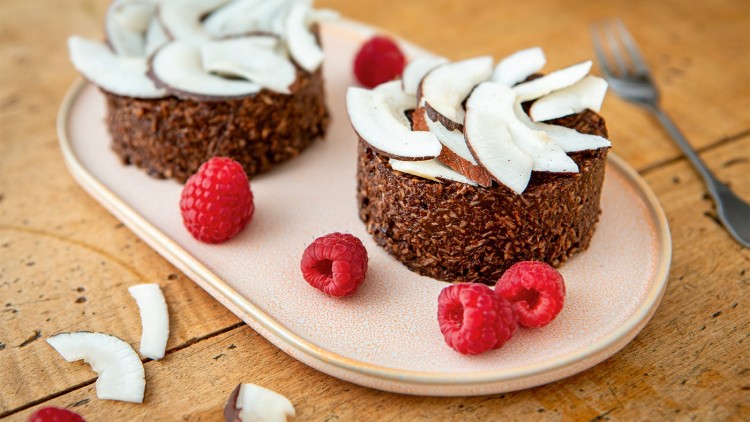 Zwei Schokodesserts mit Kokosflocken und -scheiben garniert, dekoriert mit frischen Himbeeren, auf einem Keramikteller.