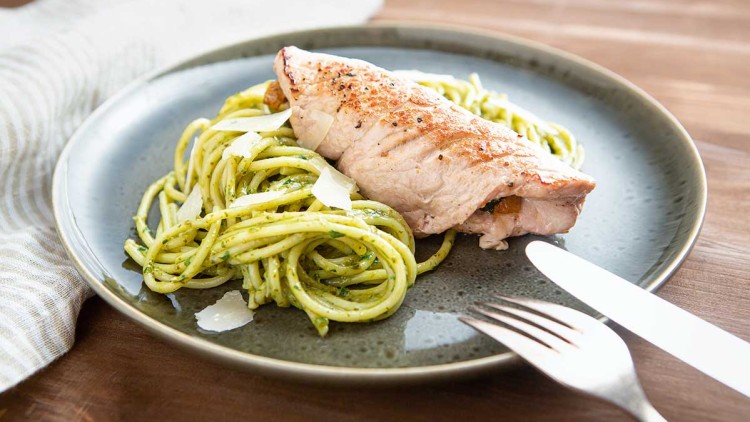 Gebratene Hähnchenbrust auf grünem Pesto-Spaghetti-Nest mit Parmesanscheiben auf einem dunkelgrünen Teller.