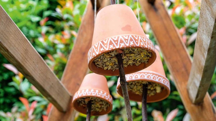 Drei mit Mustern bemalte umgedrehte Tontöpfe sind auf Ästen befestigt und mit Vogelfutter gefüllt.
