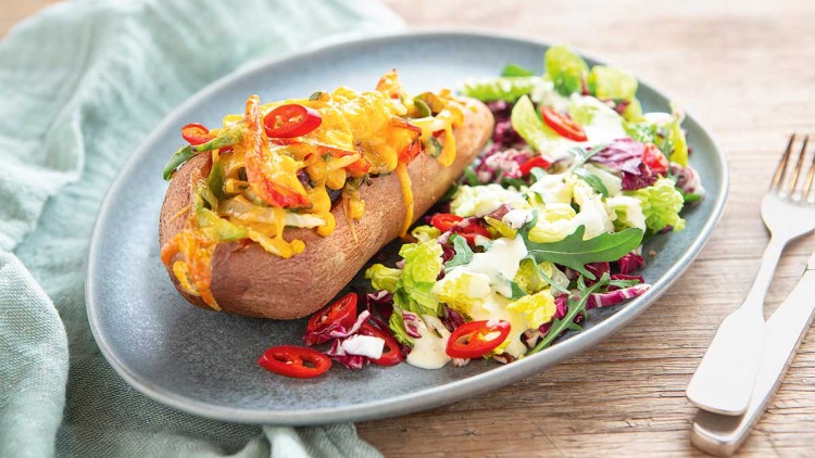 Gebackene Süßkartoffel mit überbackenem Gemüse und Chiliringen, daneben ein frischer Blattsalat mit Dressing auf grauem Teller.