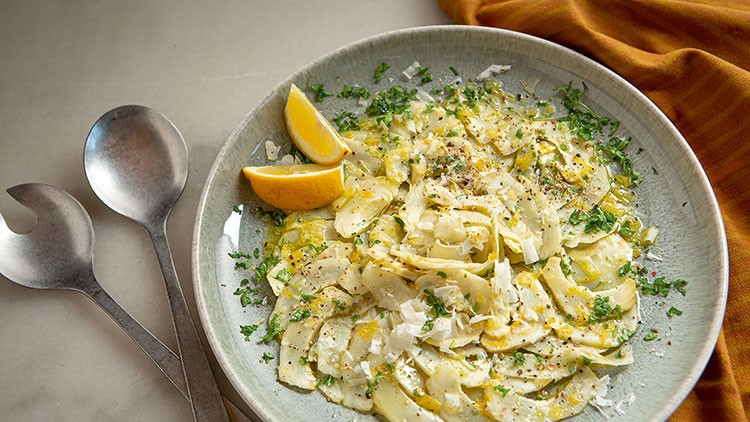 Flacher Teller mit Fenchelsalat, Kräutern, Parmesan, Pfeffer, Zitronenspalten und zwei silbernen Salatbestecken daneben.