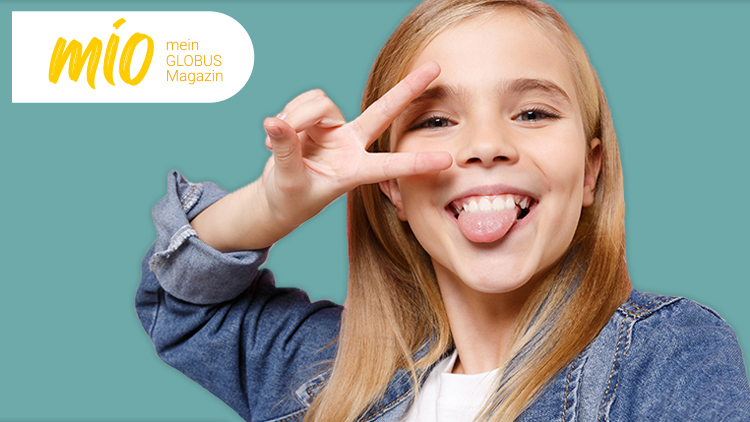 Person in jeansblauer Kleidung hält die Hand in einer Finger-Herz-Geste vor einem grünen Hintergrund, mio mein GLOBUS Magazin.