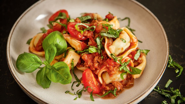 Gefüllte Nudeln mit Tomatensauce, frischem Basilikum und Kirschtomaten auf einem hellen Teller, dekoriert mit Basilikumblättern.